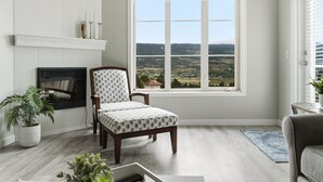 Una sala de estar con chimenea, un ventanal con vistas, un sillón estampado y una planta en maceta.