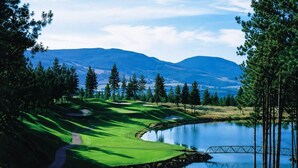Un campo de golf con un lago, árboles y montañas al fondo.