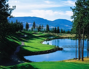 A golf course with a lake, trees, and mountains in the background. - Pinnacle Pointe | Valley-View Golf Escape (Kelowna)