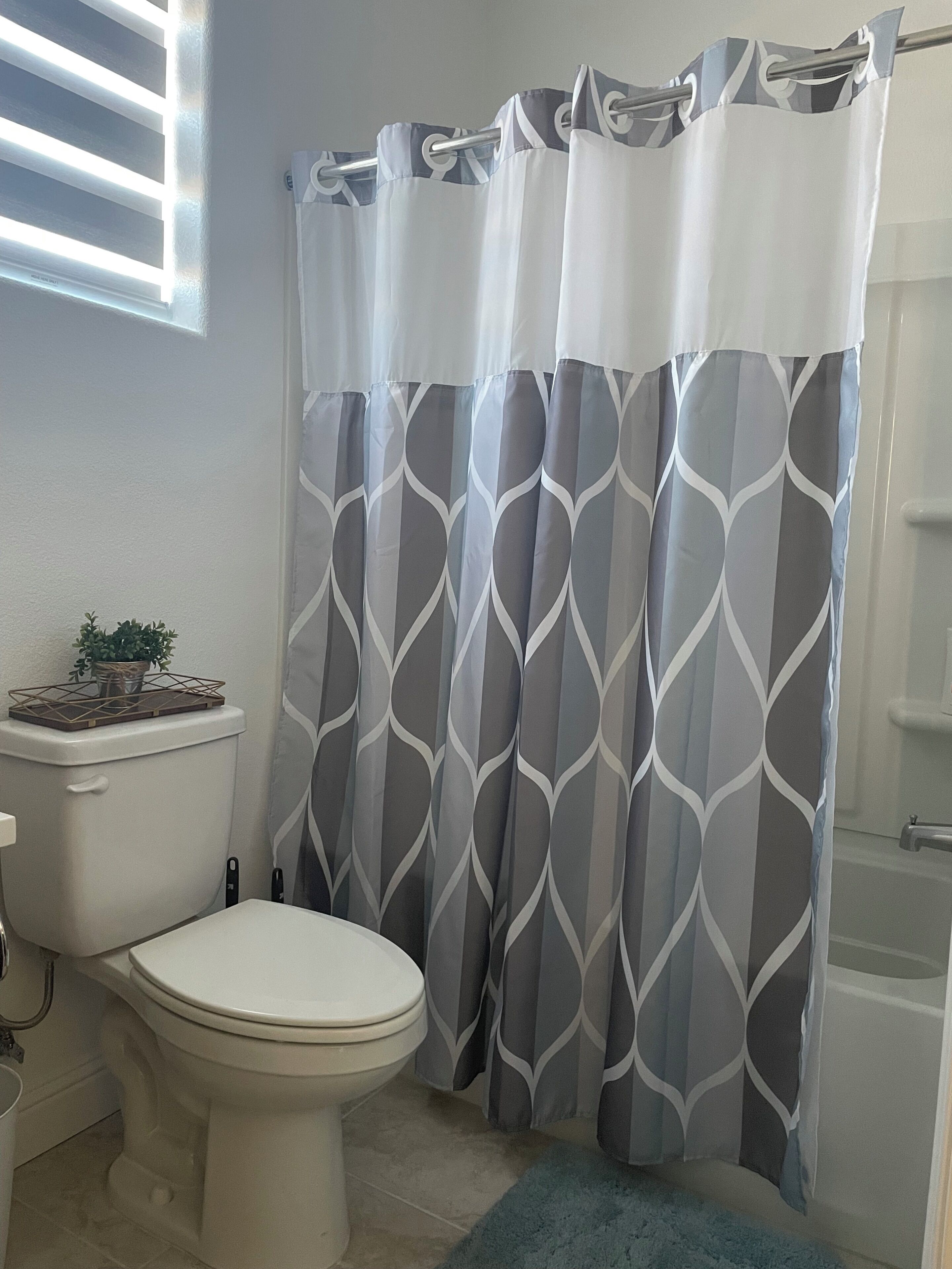 Un baño con inodoro, cortina de ducha estampada con un diseño geométrico y una alfombra de baño azul.
