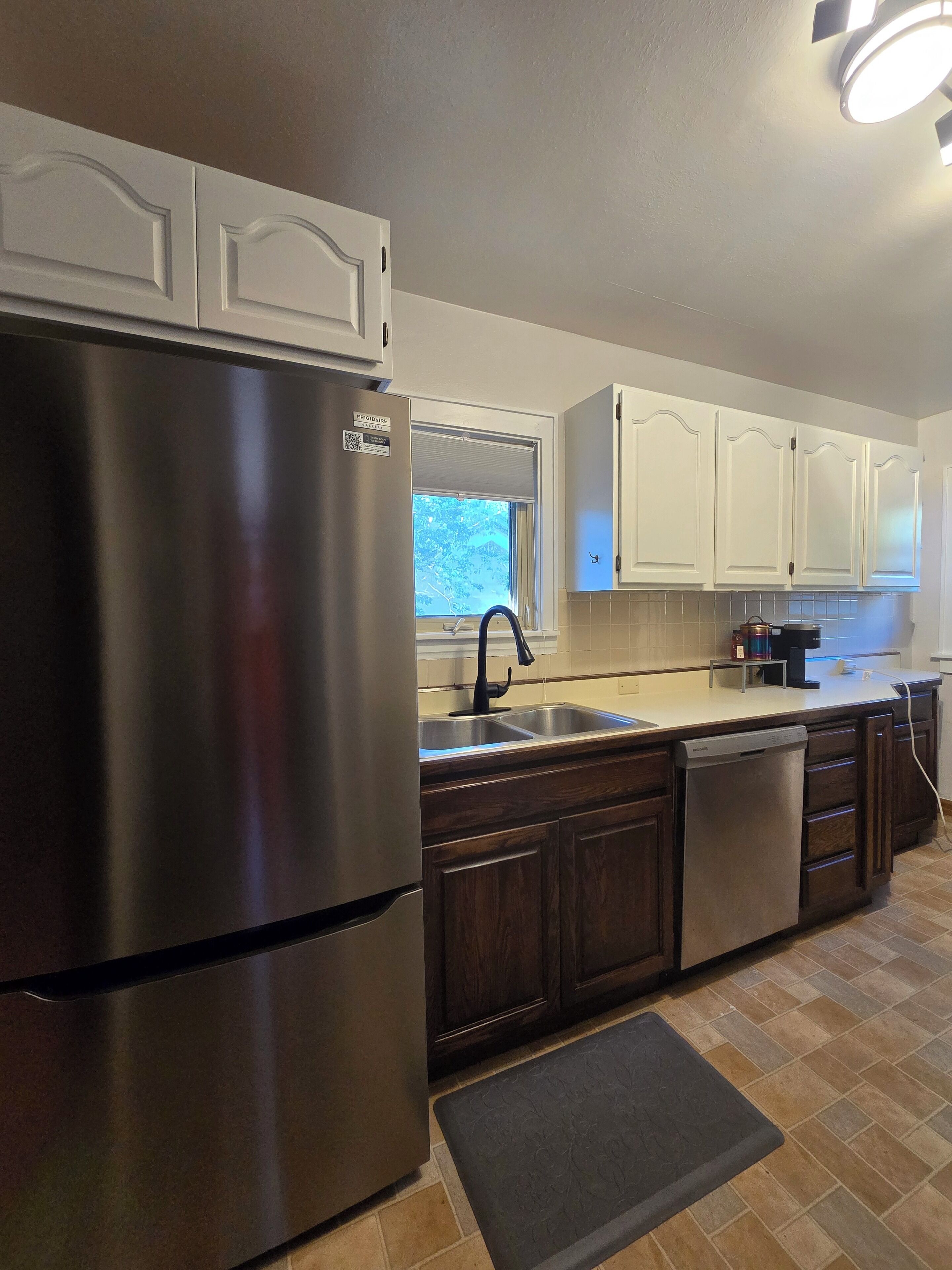 A kitchen with a stainless steel refrigerator, a double sink, and wooden cabinets.