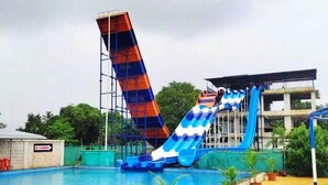 A swimming pool with two water slides, one blue and one red, and a building in the background. - Palette Virar Mumbai (Vasai)