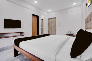 Ein modernes Hotelzimmer mit einem großen Bett, einem flachbildfernseher an der Wand, einem Nachttisch aus Holz und einem kleinen Nachttisch mit Tablett.