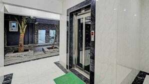 A modern lobby with a marble floor, a glass elevator, and a palm tree.