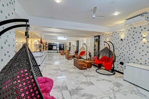 En modern hotellobby med högt i tak, marmorgolv och en sittgrupp med hängstolar.
