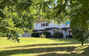 Une maison avec un patio couvert, une pelouse et un arbre au premier plan.