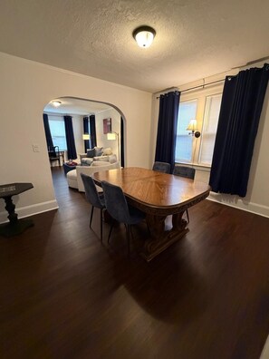 A dining area with a wooden table and chairs, a small table with a lamp, and a view of a living room through an archway. - San Marco Courtyard Retreat, a Peaceful 2-Bedroom Apartment in Jacksonville (Jacksonville)