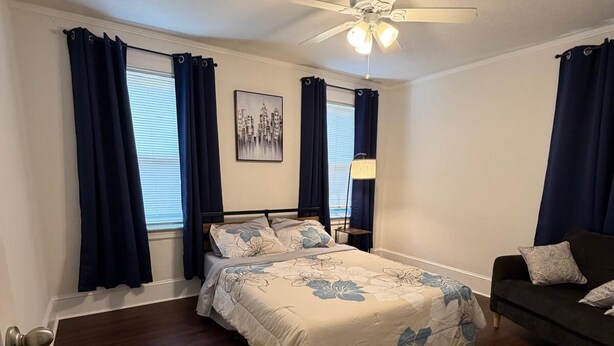 A bedroom with a bed, a nightstand, a ceiling fan, and a window with curtains. - San Marco Courtyard Retreat, a Peaceful 2-Bedroom Apartment in Jacksonville (Jacksonville)