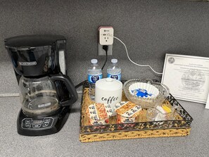 A coffee maker, two water bottles, a coffee mug, a basket with snacks, and a certificate on a countertop. - San Marco Courtyard Retreat, a Peaceful 2-Bedroom Apartment in Jacksonville (Jacksonville)