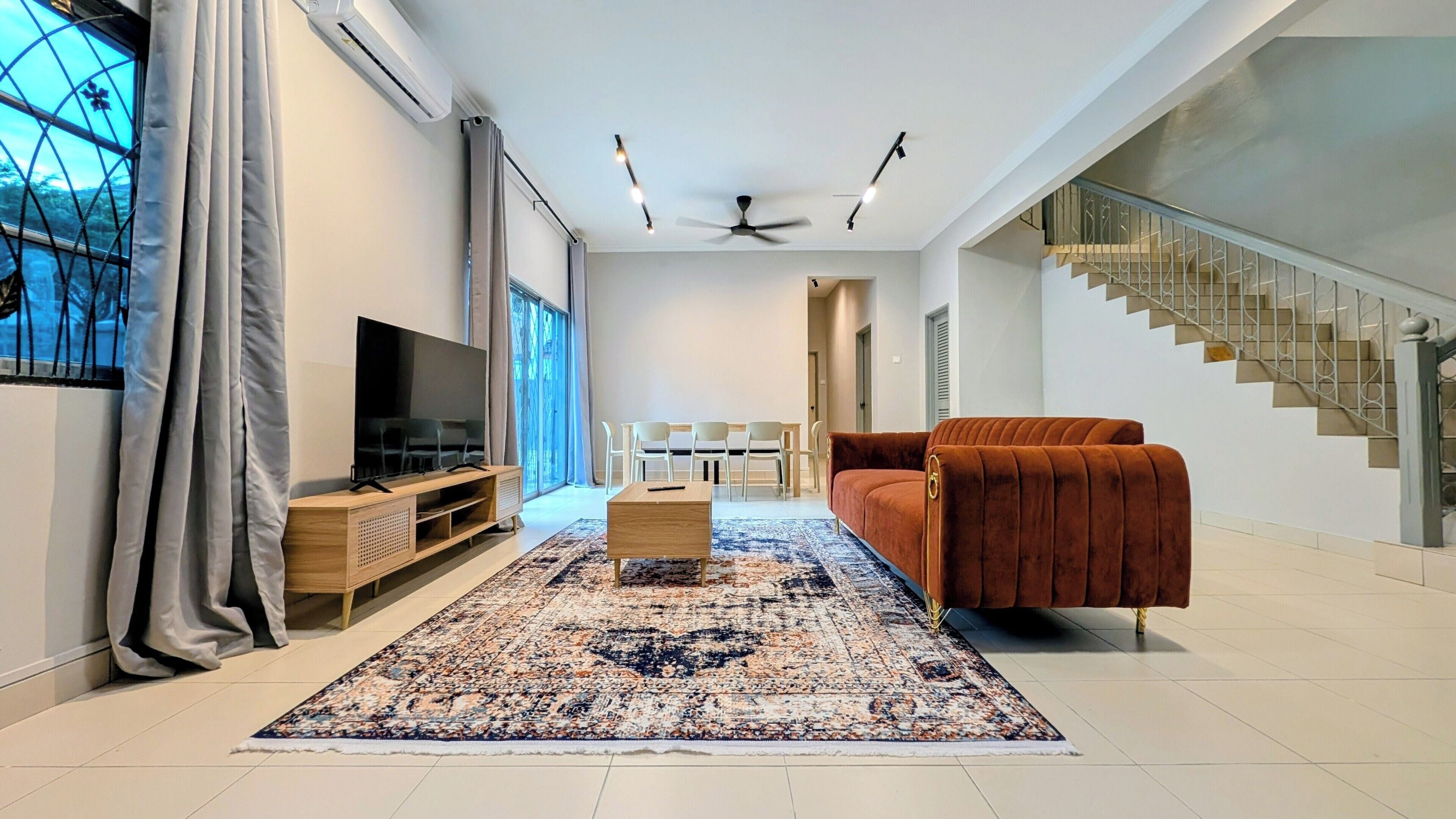 A modern living room with a flat-screen TV, a brown sofa, a coffee table, and a patterned rug.
