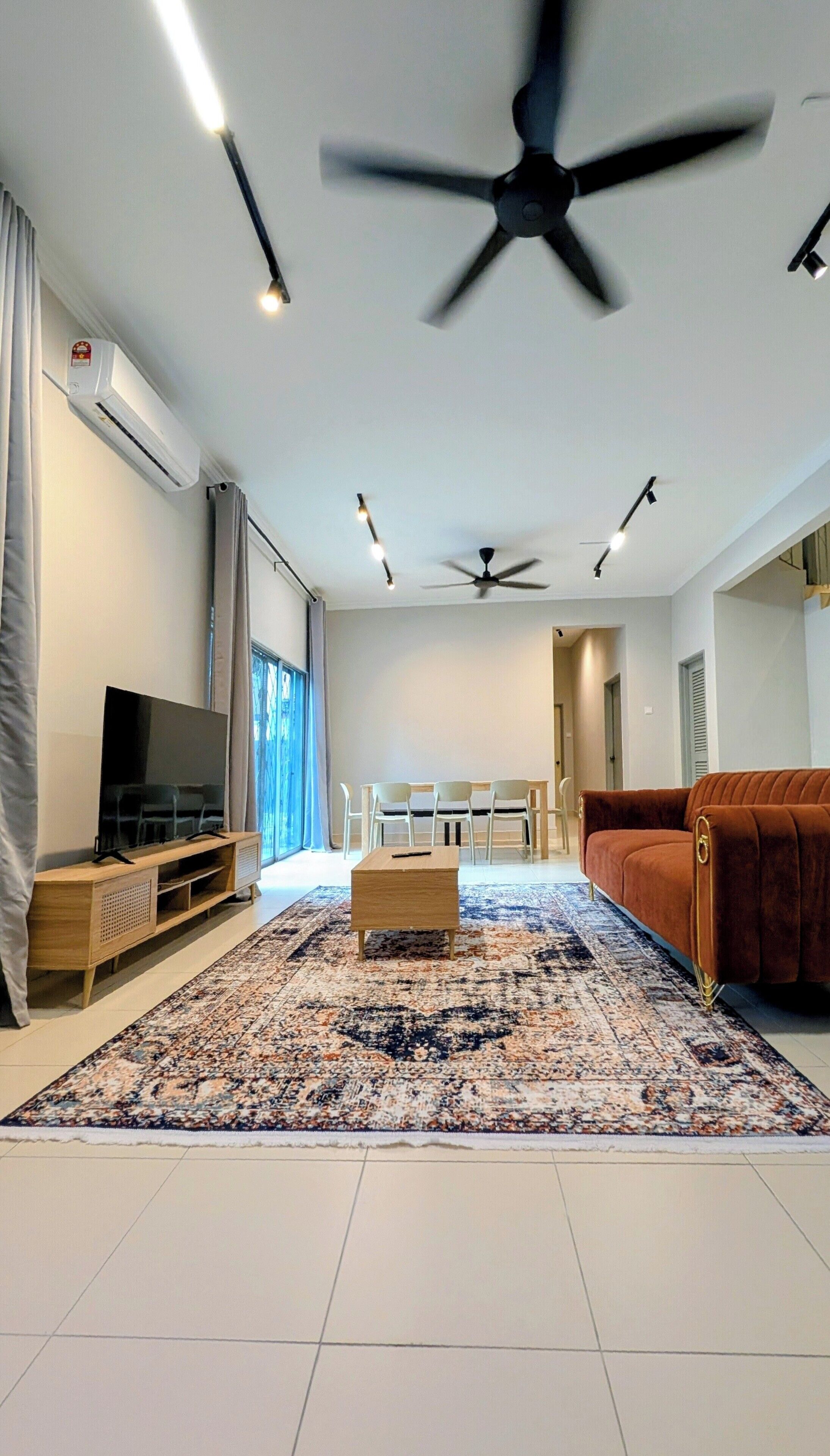 Un salon moderne doté d’un téléviseur à écran plat, de ventilateurs de plafond, d’un tapis à motifs et d’un canapé marron.