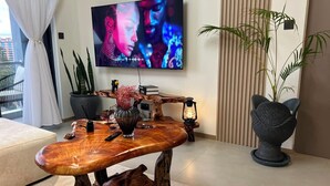 Un salon moderne avec une table basse en bois, un téléviseur à écran plat, une plante en pot et un fauteuil original.