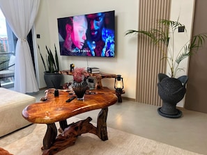 Ein stilvolles Wohnzimmer mit Couchtisch aus Holz, Flachbildfernseher, Blumentopf und einem außergewöhnlichen Sessel.