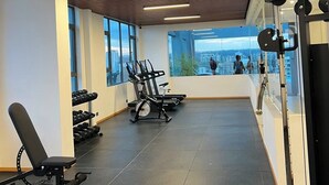 Une salle de sport équipée de matériel d’exercice, dotée de grandes fenêtres et offrant une vue sur la ville.