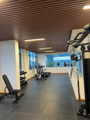 Ein Fitnessstudio mit Trainingsgeräten, großen Fenstern und Blick auf die Stadt.