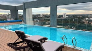 Une piscine à débordement située sur le toit, avec des chaises longues et une vue sur la ville.