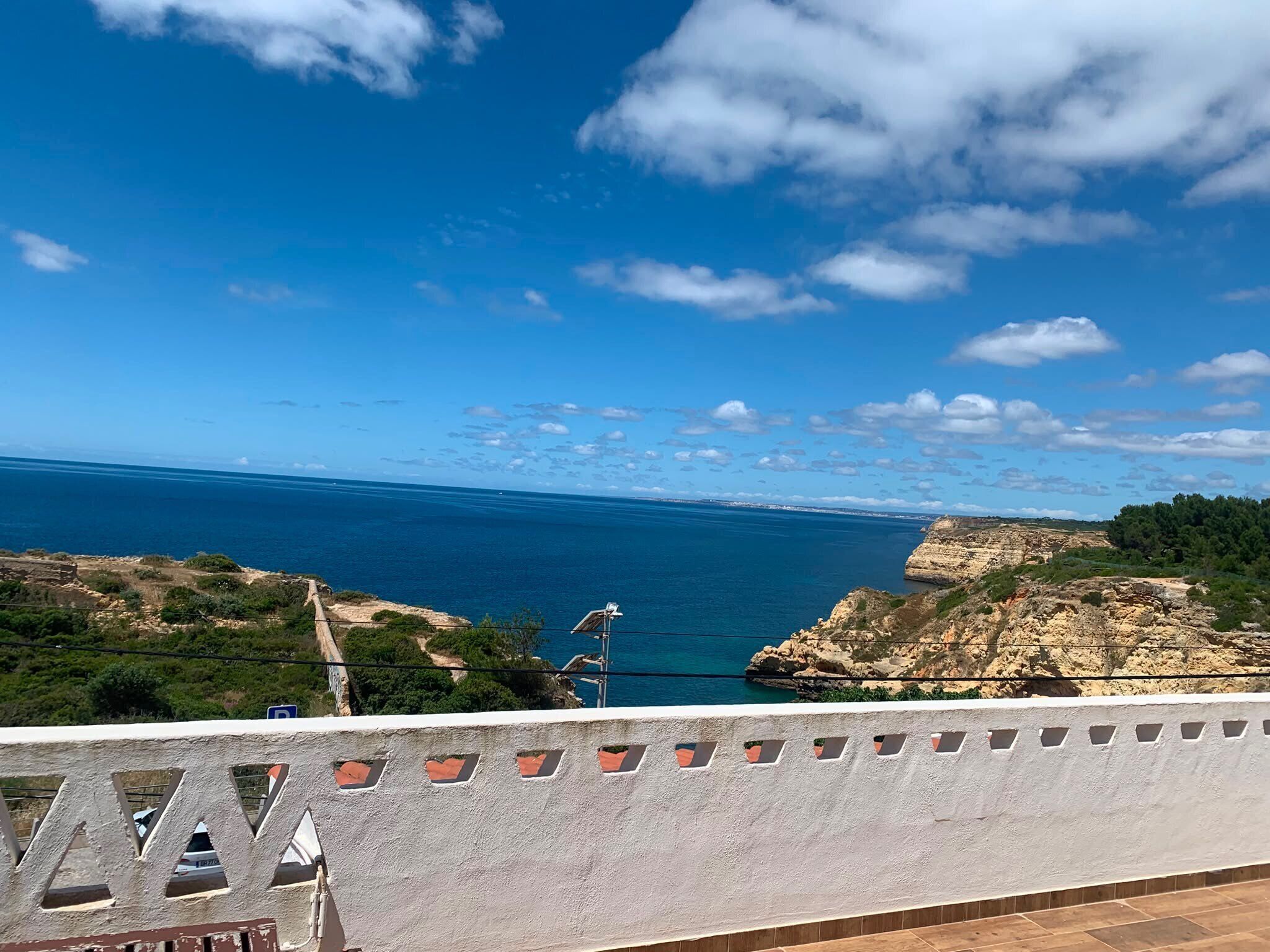 A coastal view with a clear sky, rocky terrain, and a distant shoreline.