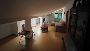 En rummelig loftrum med højt til loftet, et spiseområde med et rundt bord, en sofa og en stenvæg med et vindue.