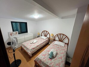 A bedroom with two single beds, a desk, a chair, a standing fan, and a window with blinds. - Sleeps4-familyfriendly-balcony (Lagoa)