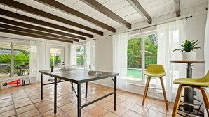 En rummelig stue med et pingpongbord, store vinduer og udsigt til en swimmingpool.