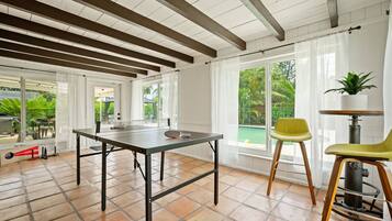 Une pièce spacieuse équipée d’une table de ping-pong, de grandes fenêtres et offrant une vue sur une piscine.