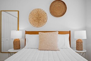Ein Schlafzimmer mit Holz-Kopfteil, weißer Bettwäsche, zwei Nachttischlampen und Wandbehängen aus Gewebe.