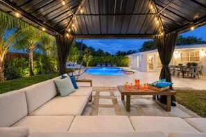 Area relax esterna coperta con piscina, poltrona a sdraio e tavolo con bevande.