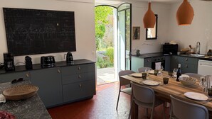 Cuina moderna amb un menú escrit a la pissarra, taula de dinar a punt per a quatre persones i vista al jardí per la porta oberta.