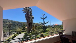 Ein Balkon mit Blick auf eine grüne Landschaft, Bäume und einen Hügel.