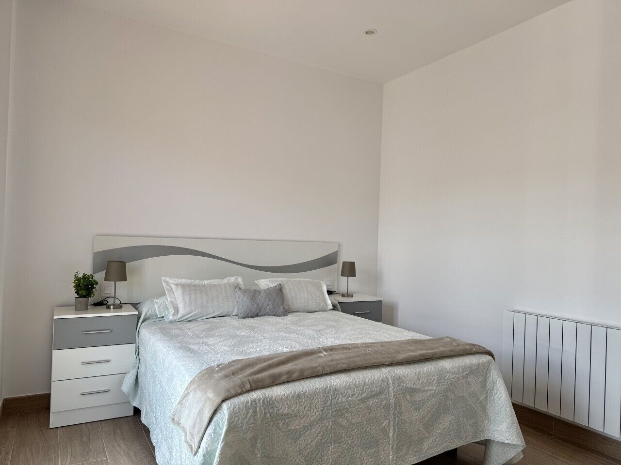 A bedroom with a bed, bedside tables, and a radiator.