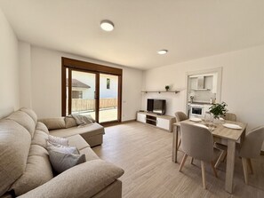 Ein modernes Wohnzimmer mit einer Couch, einem Esstisch mit Stühlen, einem Fernseher und einer Küchenzeile.