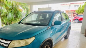 Ein blauer SUV steht in einem Gebäude mit Fliesenboden, draußen ist ein rotes Auto sichtbar.