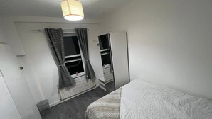 Et soveværelse med seng, gardiner ved vinduet, en radiator og et klædeskab.