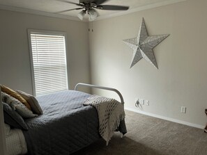 Un dormitorio con cama, ventilador de techo, ventana con persianas y un adorno de estrella en la pared.