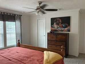Un dormitorio con cama, cómoda, ventilador de techo, puerta y ventana con persianas.