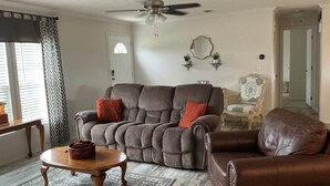 Una sala de estar con un sillón reclinable, una mesa de centro, un ventilador de techo y un espejo decorativo.