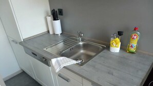 Een moderne keuken met een roestvrijstalen spoelbak, een rol keukenpapier, een fles afwasmiddel en een afwasborstel.