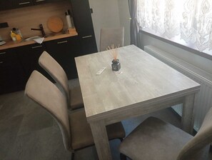 Ein Essbereich mit Tisch, Stühlen, einer kleinen Vase mit Ästen und einer Küche im Hintergrund.