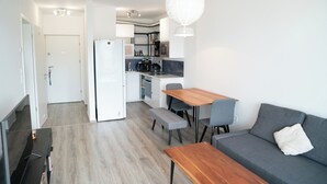 Un ambiente compatto con angolo cottura, zona pranzo con tavolo e sedie in legno e un divano grigio.