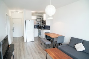 A compact living space with a kitchenette, a dining area with a wooden table and chairs, and a grey sofa. - Waterfront City Buda Hills Views&Free parking (budapest)