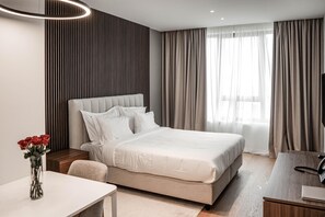 Ein modernes Hotelzimmer mit einem großen Bett, Nachttischen, einem Schreibtisch und einem Blumenstrauß.