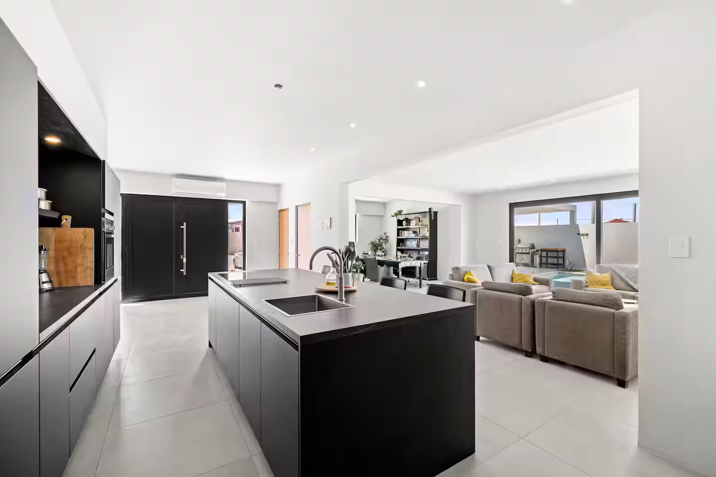 A modern kitchen with a central island, a dining area with a sofa, and a view of the outdoors.