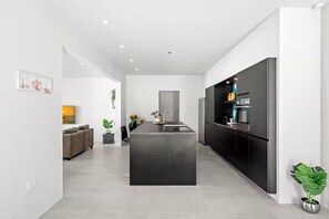 Une cuisine moderne dotée d’un îlot central, de meubles de couleur noire et d’un coin repas avec un canapé et des plantes.