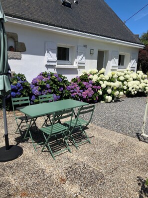 A white house with a gravel driveway, a green table and chairs, and a variety of flowers. - Family home with exceptional view of the Gulf of Morbihan - Sleeps 8 (Arzon)