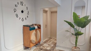 A hallway with a wall clock, a wooden cabinet, a patterned rug, and a potted plant. - Diarna Downtown Residency (Marsa Matrouh Governorate)