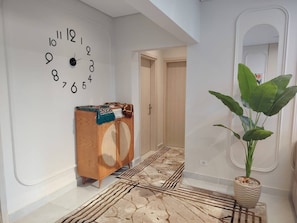 A hallway with a wall clock, a wooden cabinet, a patterned rug, and a potted plant.