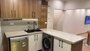 A compact kitchen with wooden cabinets, a dishwasher, a washing machine, and a countertop. - Diarna Downtown Residency (Marsa Matrouh Governorate)