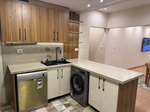 A compact kitchen with wooden cabinets, a dishwasher, a washing machine, and a countertop.