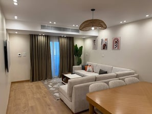 A modern living room with a sofa, a dining table, a TV, and a large window with curtains.