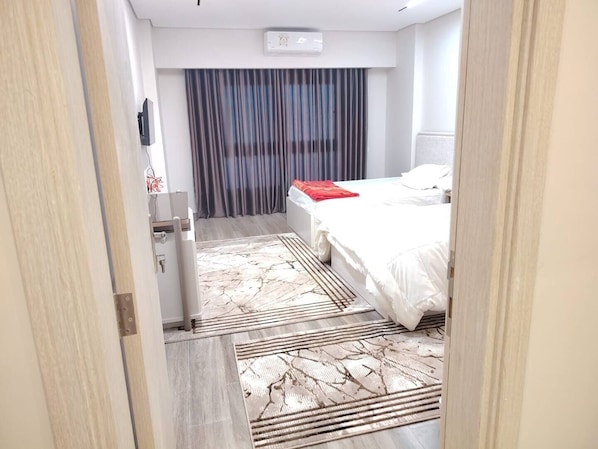A hotel room with a bed, a desk, a chair, a window with curtains, and a door.